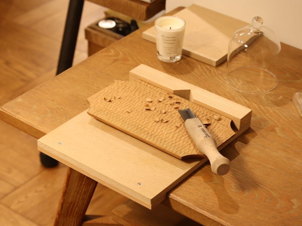 【東京・西東京】山桜の木工ワークショップ|手作りカフェトレーとお茶会の時間(くらテク・マルシェ) 東京・西東京市の「岡庭建設」にて開催される、木工ユニット「mutou」による山桜のカフェトレー製作ワークショップの様子。国産の山桜の天然木を彫刻刀で無心に削り、自分だけの削り跡を刻んでいく。フラット面と削り跡面の、ふたつの表情をあわせ持つトレー。 製作の後には、食用としても知られる安心な「くるみオイル」で仕上げる。 仕上がったばかりの自分だけのトレーとお気に入りの器で、手仕事の余韻に浸る穏やかなお茶会。木の心地よさや、日々の暮らしのこと。穏やかにお話ししながら、自分へのご褒美時間を。初心者でも安心の少人数制。専門講師(mutou)による丁寧なサポート。